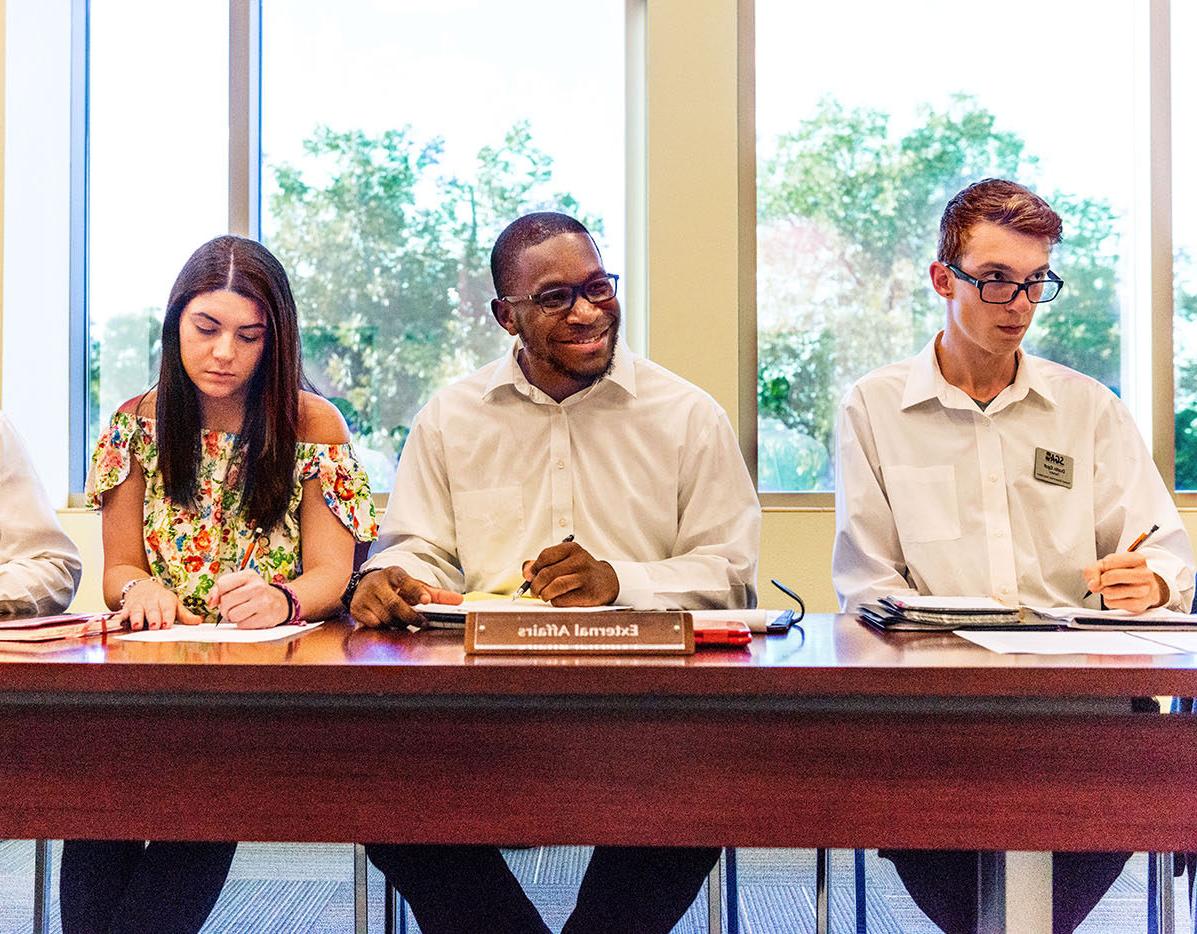 在一次学生会会议上，两名男学生和一名女学生坐在一张桌子旁.